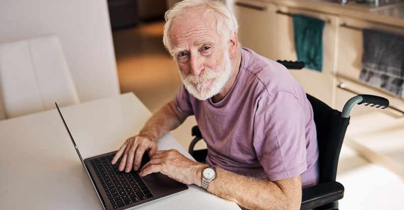 A senior in a wheelchair is sitting at the computer.