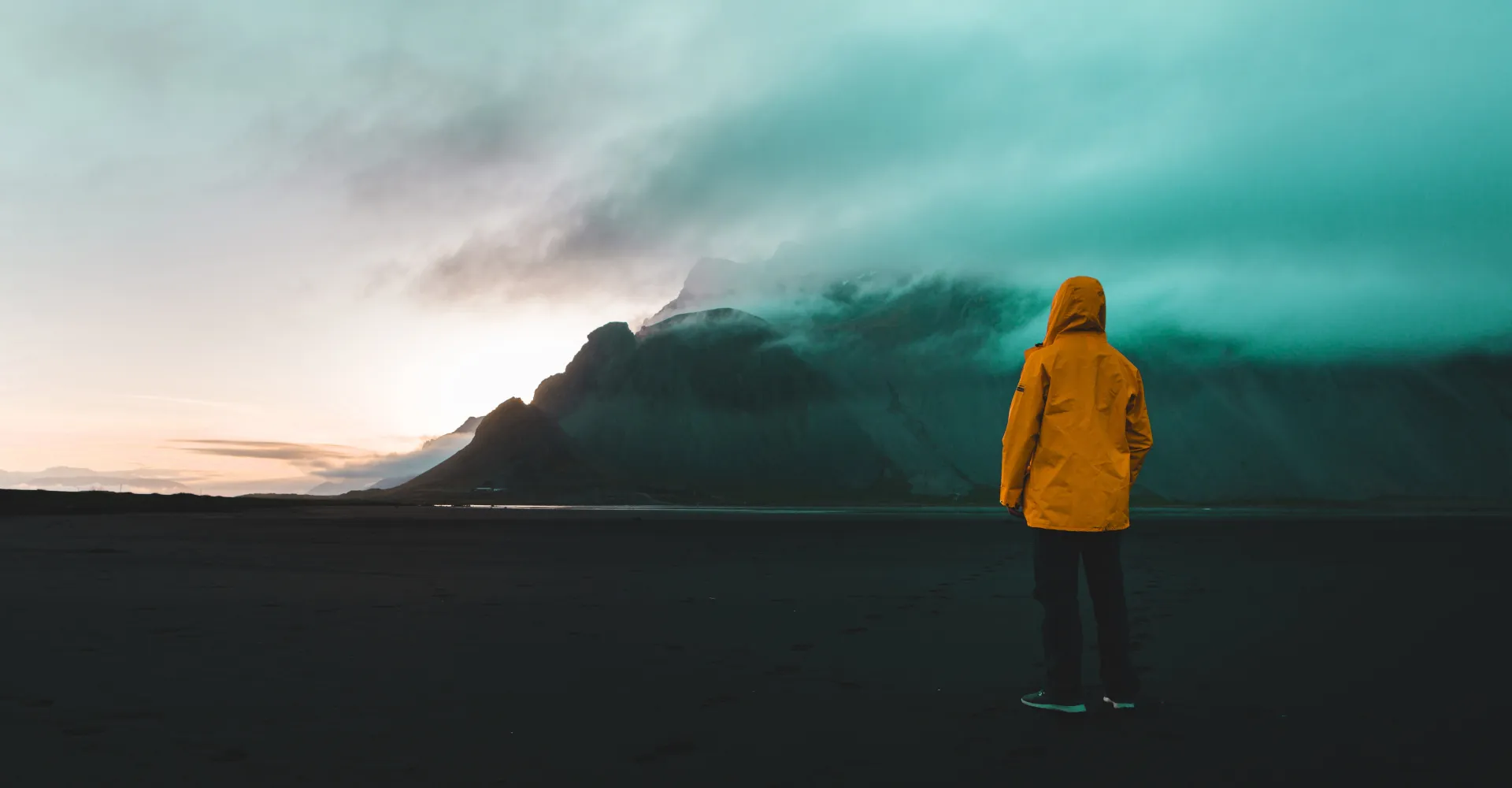 A man in a yellow rain jacket looking at dark clouds in the distance.